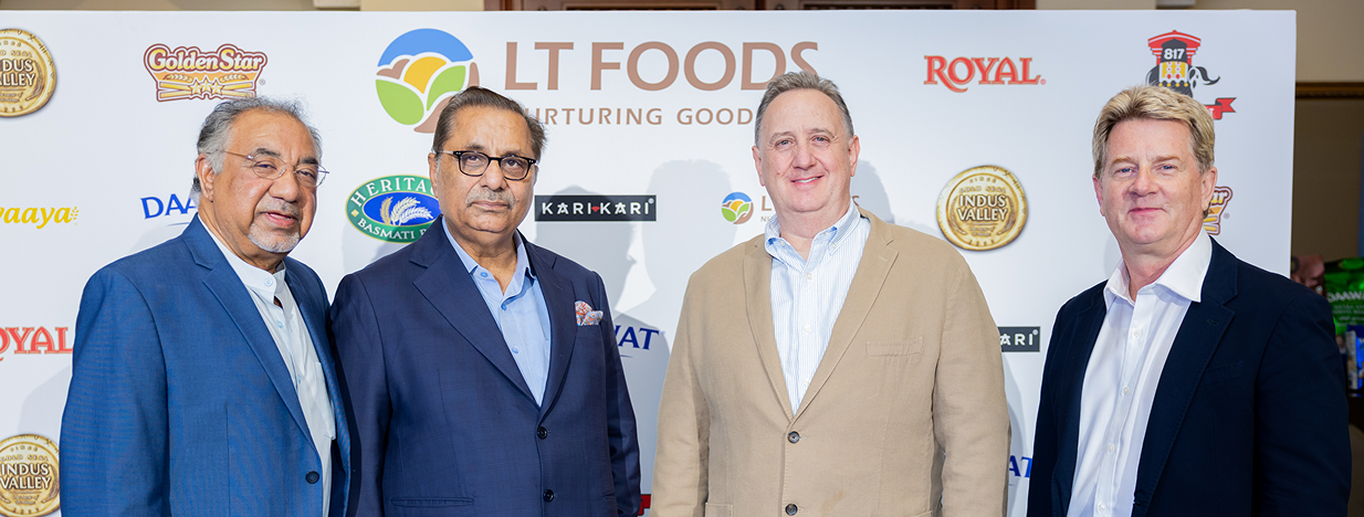 Executives posing in front of an LT Foods brand backdrop featuring Daawat, Royal, Heritage, and other company brands during a corporate event.